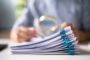 a stack of patent documents with a man using a magnifying glass